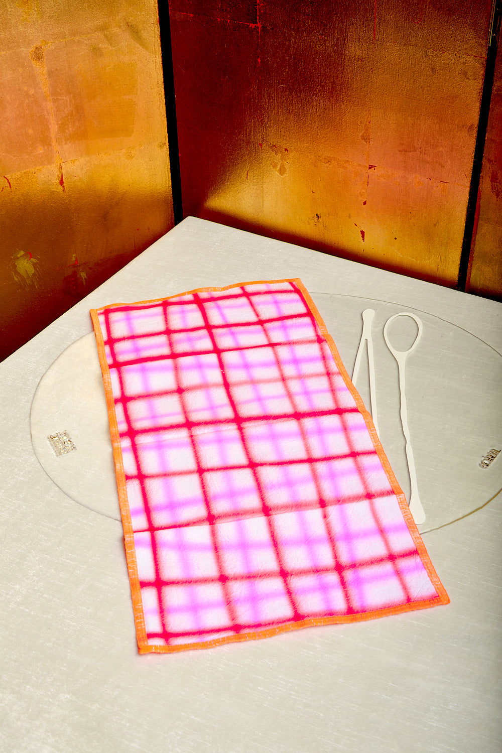 A vibrant red and neon pink napkin by Hotel Elma with neon orange trim is draped across a transparent placemat by Gaetano Pesce for Fish Design.